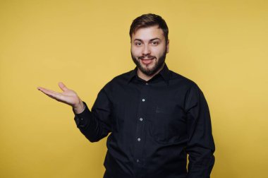 Siyah gömlekli neşeli bir adam canlı sarı bir arkaplan karşısında duruyor, elini uzatıyor sanki konuşmaya davet ediyormuş gibi. Onun dostane ifadesi sahneye sıcaklık getiriyor..