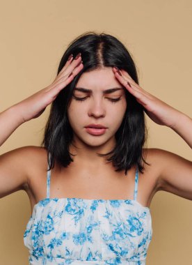 A young woman with dark hair shows a pained expression, holding her head in her hands. The plain yellow background adds to her sense of frustration and contemplation.