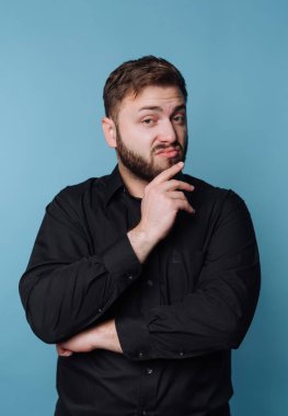 Sakallı bir adam bir sonraki hamlesini düşünürken bir eli çenesinde duruyor. Parlak mavi arka plan, onun garip davranışlarını ve hayal gücünü ön plana çıkarıyor..