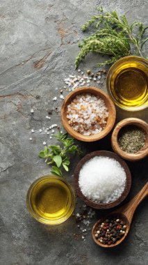 Top view flat lay of kitchen seasonings salt, pepper, oil, vinegar, and herbs on rustic countertop with copy space, warm natural light, cooking preparation concept, clean realistic style for website or print use.