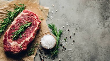 Top view flat lay of raw steak, rosemary, salt, and pepper on rustic background with copy space, soft natural light, realistic texture, cooking preparation concept, clean professional style for website or print.