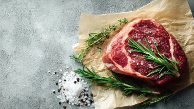 Top view flat lay of raw steak, rosemary, salt, and pepper on rustic background with copy space, soft natural light, realistic texture, cooking preparation concept, clean professional style for website or print.