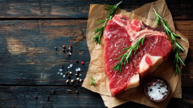 Top view flat lay of raw T-bone steak with rosemary, salt, and pepper on rustic wooden background with copy space, warm natural light, realistic texture, gourmet cooking concept, professional style for website or print use.