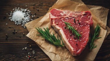 Top view flat lay of raw T-bone steak with rosemary, salt, and pepper on rustic wooden background with copy space, warm natural light, realistic texture, gourmet cooking concept, professional style for website or print use.