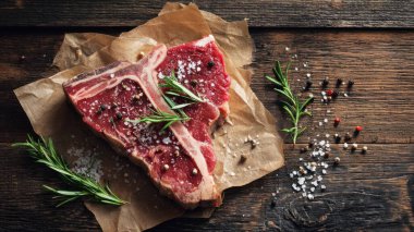 Top view flat lay of raw T-bone steak with rosemary, salt, and pepper on rustic wooden background with copy space, warm natural light, realistic texture, gourmet cooking concept, professional style for website or print use.