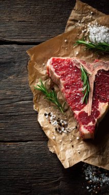 Top view flat lay of raw T-bone steak with rosemary, salt, and pepper on rustic wooden background with copy space, warm natural light, realistic texture, gourmet cooking concept, professional style for website or print use.