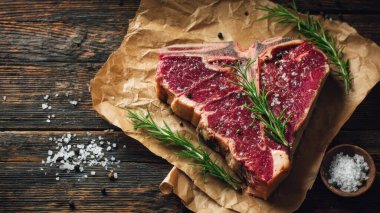 Top view flat lay of raw T-bone steak with rosemary, salt, and pepper on rustic wooden background with copy space, warm natural light, realistic texture, gourmet cooking concept, professional style for website or print use.