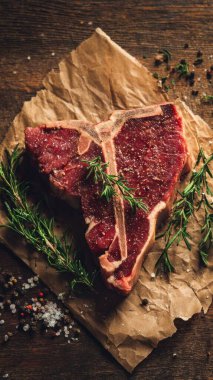 Top view flat lay of raw T-bone steak with rosemary, salt, and pepper on rustic wooden background with copy space, warm natural light, realistic texture, gourmet cooking concept, professional style for website or print use.