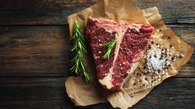 Top view flat lay of raw T-bone steak with rosemary, salt, and pepper on rustic wooden background with copy space, warm natural light, realistic texture, gourmet cooking concept, professional style for website or print use.