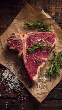 Top view flat lay of raw T-bone steak with rosemary, salt, and pepper on rustic wooden background with copy space, warm natural light, realistic texture, gourmet cooking concept, professional style for website or print use.
