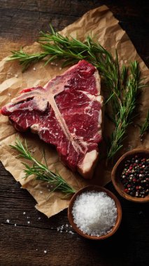 Top view flat lay of raw T-bone steak with rosemary, salt, and pepper on rustic wooden background with copy space, warm natural light, realistic texture, gourmet cooking concept, professional style for website or print use.