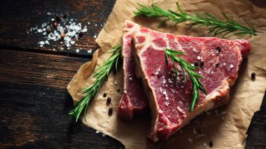 Top view flat lay of raw T-bone steak with rosemary, salt, and pepper on rustic wooden background with copy space, warm natural light, realistic texture, gourmet cooking concept, professional style for website or print use.