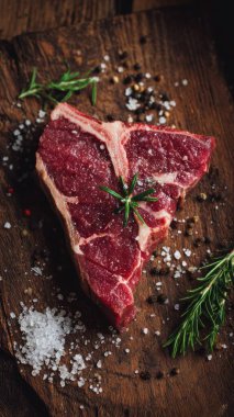 Top view flat lay of raw T-bone steak with rosemary, salt, and pepper on rustic wooden background with copy space, warm natural light, realistic texture, gourmet cooking concept, professional style for website or print use.