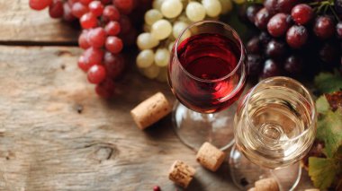 Top view flat lay of red and white wine glasses on wooden table, scattered grapes and corks, blurred background with copy space, warm natural light, elegant beverage concept, realistic style for website or print use.