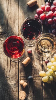 Top view flat lay of red and white wine glasses on wooden table, scattered grapes and corks, blurred background with copy space, warm natural light, elegant beverage concept, realistic style for website or print use.
