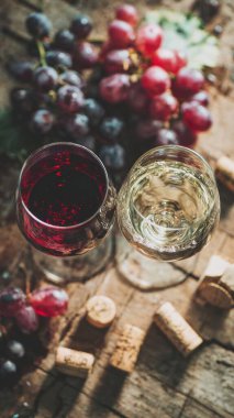 Top view flat lay of red and white wine glasses on wooden table, scattered grapes and corks, blurred background with copy space, warm natural light, elegant beverage concept, realistic style for website or print use.