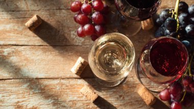 Top view flat lay of red and white wine glasses on wooden table, scattered grapes and corks, blurred background with copy space, warm natural light, elegant beverage concept, realistic style for website or print use.