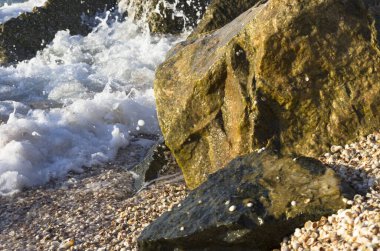 Deniz dalgaları kıyı taşlarına karışıyor.