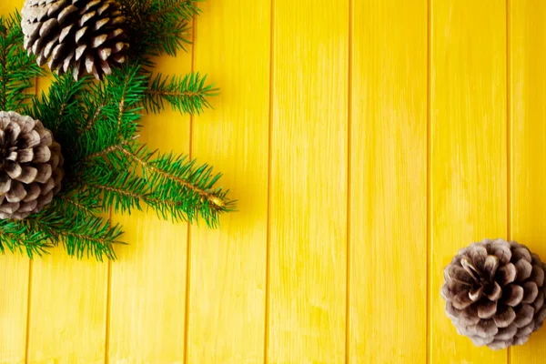 크리스마스 소나무 가지와 원추형을 낡은 노란색 나무판에 얹어 만든 틀이다. 문자를 위한 공간. 위에서 본 풍경. — 스톡 사진