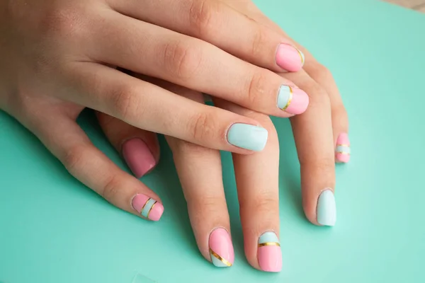 Las manos de las mujeres con una manicura elegante en verde azulado o azul y rosa Imagen De Stock