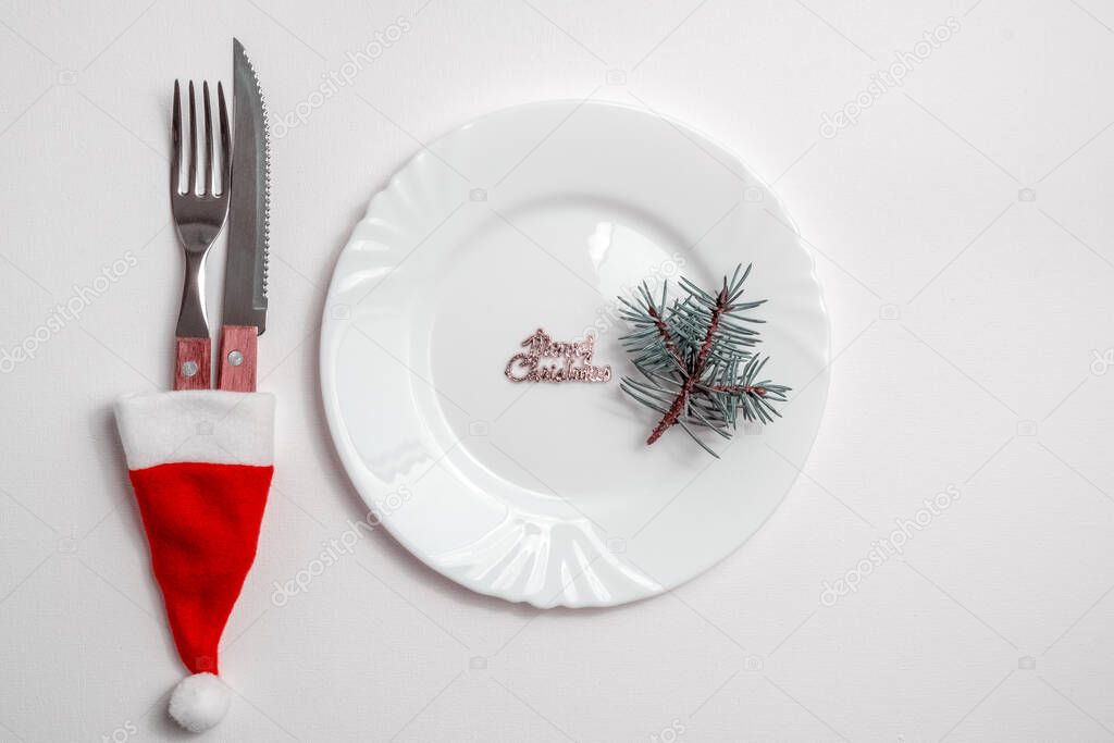 Traditional Christmas table place setting with empty white plate, linen napkin, cutlery with festive decorations. New Years background and Holiday concept. Flat lay, top view with copy space