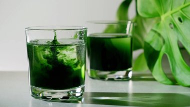 Chlorophyll extract is poured in pure water in glass against a white grey background with green leaf. Liquid chlorophyll in a glass of water. Concept of superfood, healthy eating, detox and diet clipart