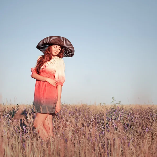 Romantiska ung kvinna i hatt står på ängen i varm sommardag — Stockfoto