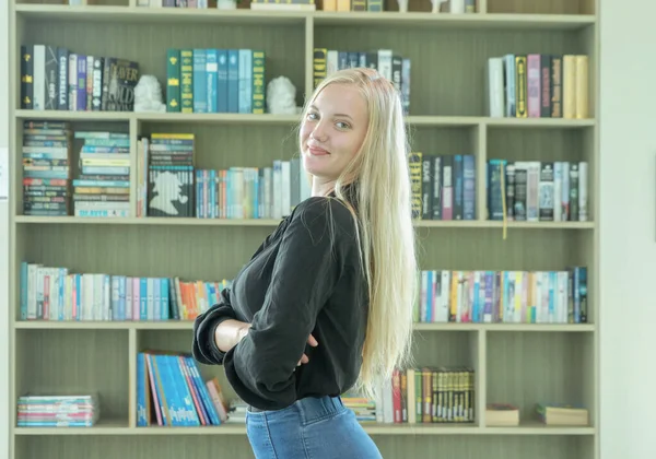 Portrait of smiling business blonde, white woman person reading a book in a library in education concept. Student studying in college, school or university.