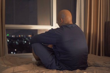 Bunalımlı, yalnız, yaşlı, yaşlı siyah adam. Afro-Amerikalı insanlar yataklarında pencereleri ve şehir manzarası olan evlerindeki yatak odalarında oturuyorlar. Gece geç saatte yaşam tarzı. Uykusuzluk. Karantina