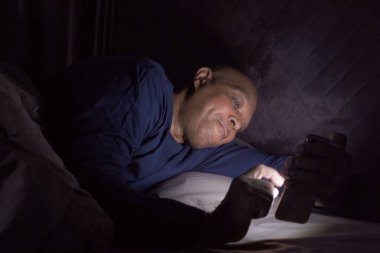 Bunalımlı yaşlı siyah adam. Sosyal medyada akıllı telefon kullanan ve yatak odasında uyuyan Afrikalı Amerikalılar. Teknoloji aygıtı konseptinde gece geç saatte yaşam tarzı. Uykusuzluk.