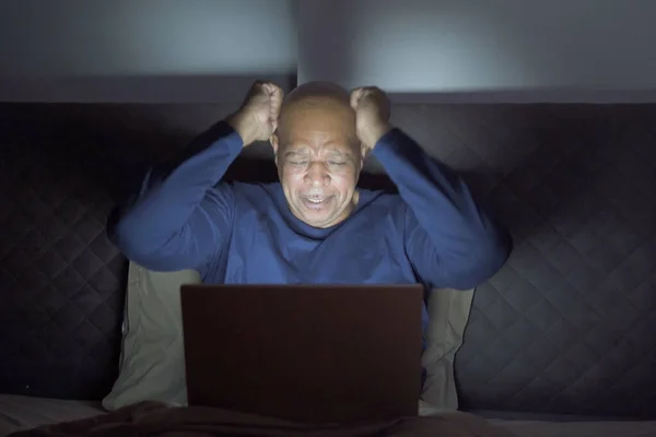 Depressed elderly black man. African American people using a notebook laptop computer on social media internet on bed in bedroom at home. Lifestyle on late night in technology device concept. Insomnia