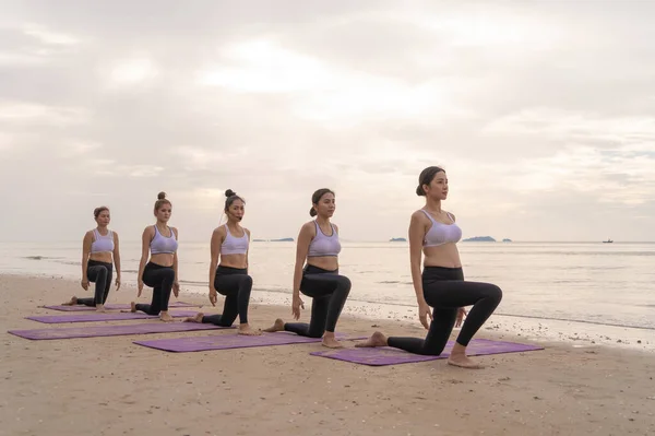 Group of Asian women in yoga class club doing exercise and yoga at natural beach and sea coast outdoor in sport and recreation concept. People lifestyle activity.