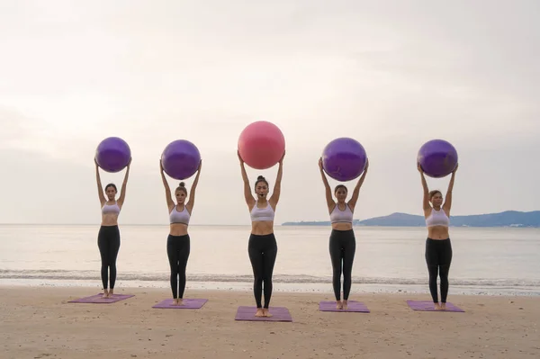 Group of Asian women in yoga class club doing exercise and yoga at natural beach and sea coast outdoor in sport and recreation concept. People lifestyle activity.