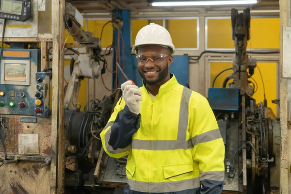 Black African American man, an engineer or worker control the smart robot welding hand system automated manufacturing machine engine in factory, industry equipment in operation warehouse. People.