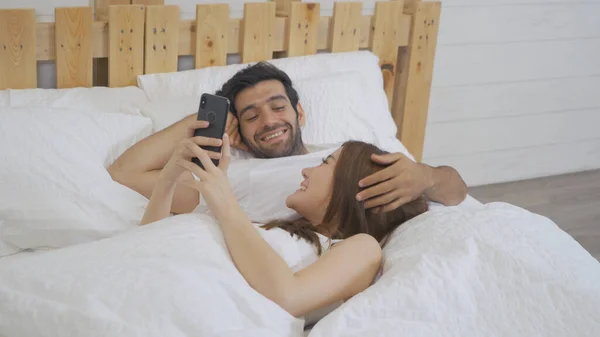 A couple family. Happy middle east young man and Asian woman. People using a smartphone on social media internet and sleeping on bed in bedroom at home. Lifestyle in technology in early. Multi ethnic