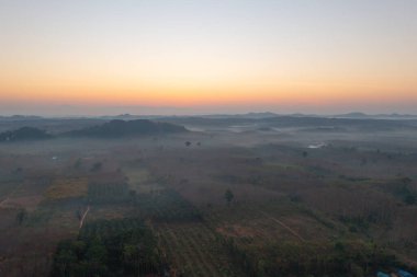Gün batımında sisli orman ağaçlarının ve yeşil dağ tepelerinin havadan görünüşü. Doğa manzarası arka planı, Tayland.