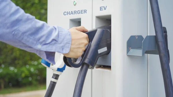 Hand pulling in cable from EV car charger or electric vehicle station. Cable connected at gas station, power supply battery charging an alternative eco environment future technology energy innovation