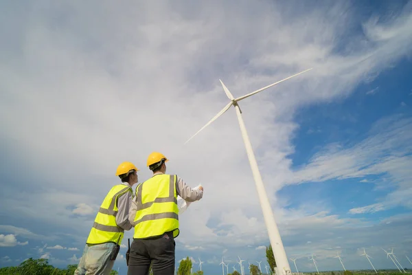 Teamwork of Asian windmill engineer group, worker working, holding a plan on site at wind turbines field or farm, clean energy source. Eco technology for electric power. industry nature. People