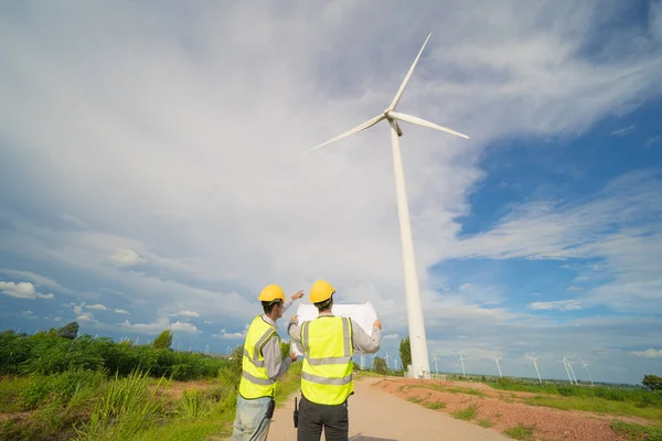 Teamwork of Asian windmill engineer group, worker working, holding a plan on site at wind turbines field or farm, clean energy source. Eco technology for electric power. industry nature. People