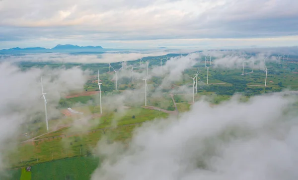 Aerial view of wind turbines or windmills farm field in industry factory with sea fog. Power, sustainable green clean energy, and environment concept. Nature innovation.