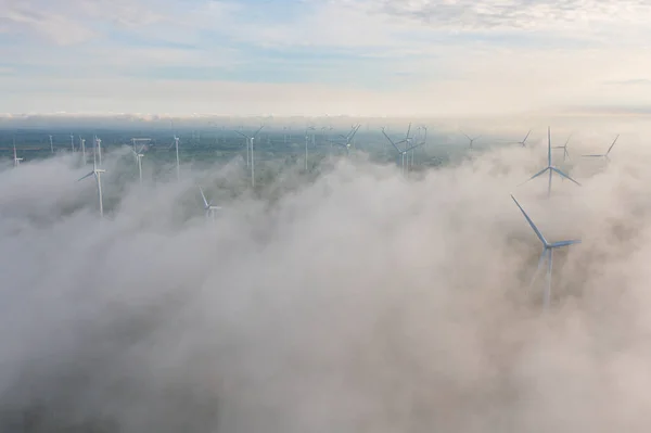 Aerial view of wind turbines or windmills farm field in industry factory with sea fog. Power, sustainable green clean energy, and environment concept. Nature innovation.