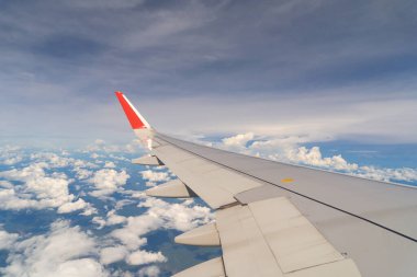 Seyahat ve ulaşım kavramında pencereden mavi gökyüzü ile bulutların üzerinde uçan bir uçak jeti kanadı. Doğa manzarası arka planı.