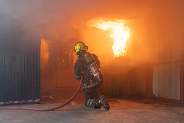 A firefighter or fireman with uniform using water fire hose against hot burning fire and dangerous smoke in the container, an emergency accident rescue. People. Hero