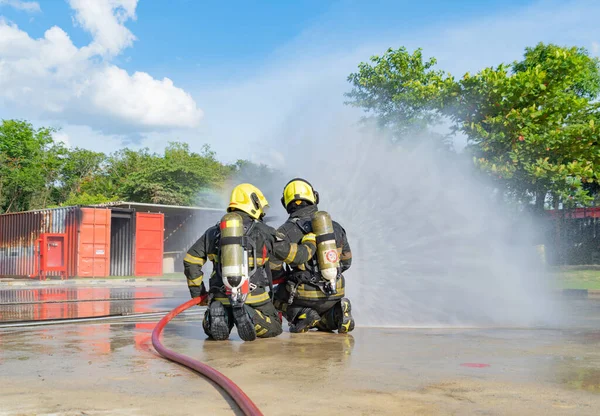 A group of firefighter or fireman with uniform using water fire hose against hot burning fire and dangerous smoke in the container, an emergency accident rescue. People. Hero teamwork.