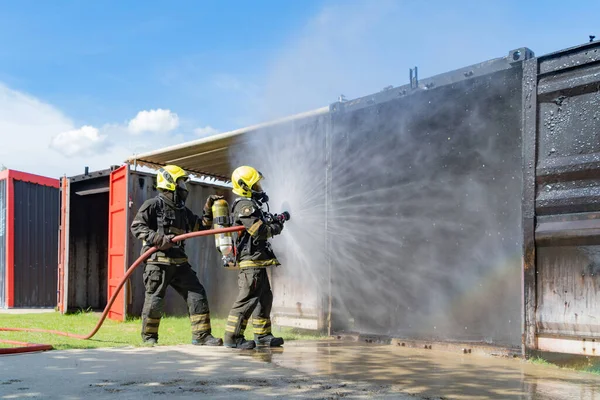 消防士や消防士のグループは コンテナ内の熱い燃焼火災や危険な煙 緊急事故救助に対して水の消防ホースを使用して均一で ヒーローチームワーク — ストック写真