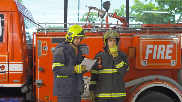 彼らのキャリアに取り組んで 均一でタブレットデバイスを持つ白人消防士や消防チームのグループ 緊急事故救助だ 消防車とヒーローのチームワーク 勤務先 — ストック写真
