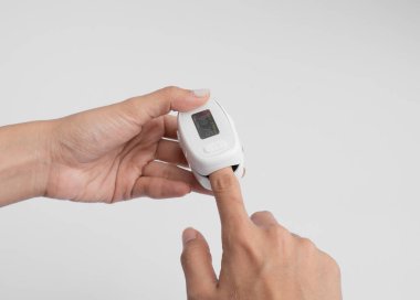 Nabız oksimetresi ya da kan oksijeni ölçme cihazı olan beyaz arka planda izole edilmiş bir el. Teşhis kendi kendini kontrol ediyor. Tıbbi ve sağlık ekipmanları. Coronavirüs covid-19 salgını.