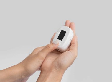 Nabız oksimetresi ya da kan oksijeni ölçme cihazı olan beyaz arka planda izole edilmiş bir el. Teşhis kendi kendini kontrol ediyor. Tıbbi ve sağlık ekipmanları. Coronavirüs covid-19 salgını.