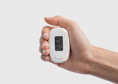 Nabız oksimetresi ya da kan oksijeni ölçme cihazı olan beyaz arka planda izole edilmiş bir el. Teşhis kendi kendini kontrol ediyor. Tıbbi ve sağlık ekipmanları. Coronavirüs covid-19 salgını.