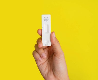 El, sarıda izole edilmiş bir test çubuğu kartuşu tutuyor. COVID-19. Hızlı otomatik test kitleri. Antijen veya antikor testi. Virüs hastalığı sağlık kontrolü. Coronavirüs salgını.